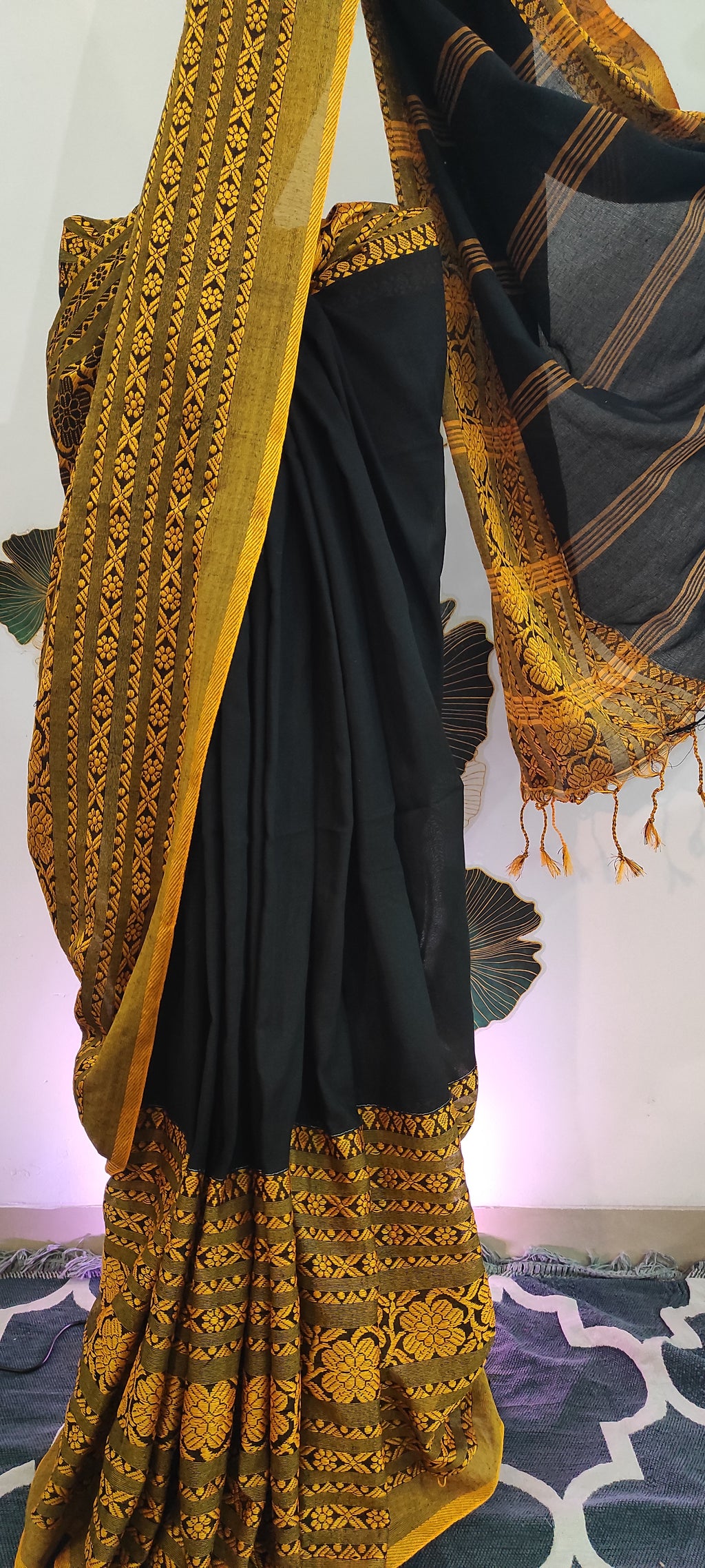 Black saree with gold embroidery on a stand against a colorful background
