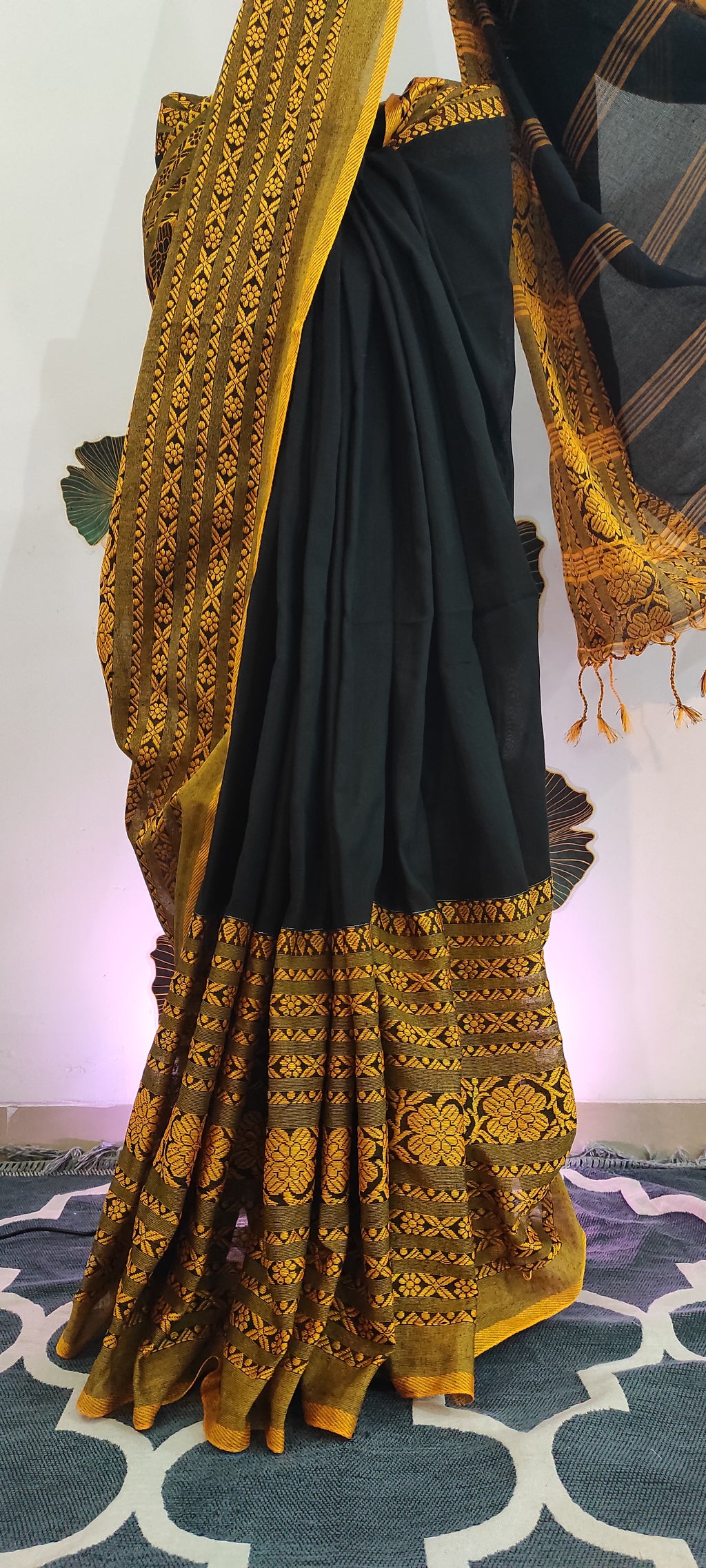 Black saree with gold embroidery on a stand against a colorful background
