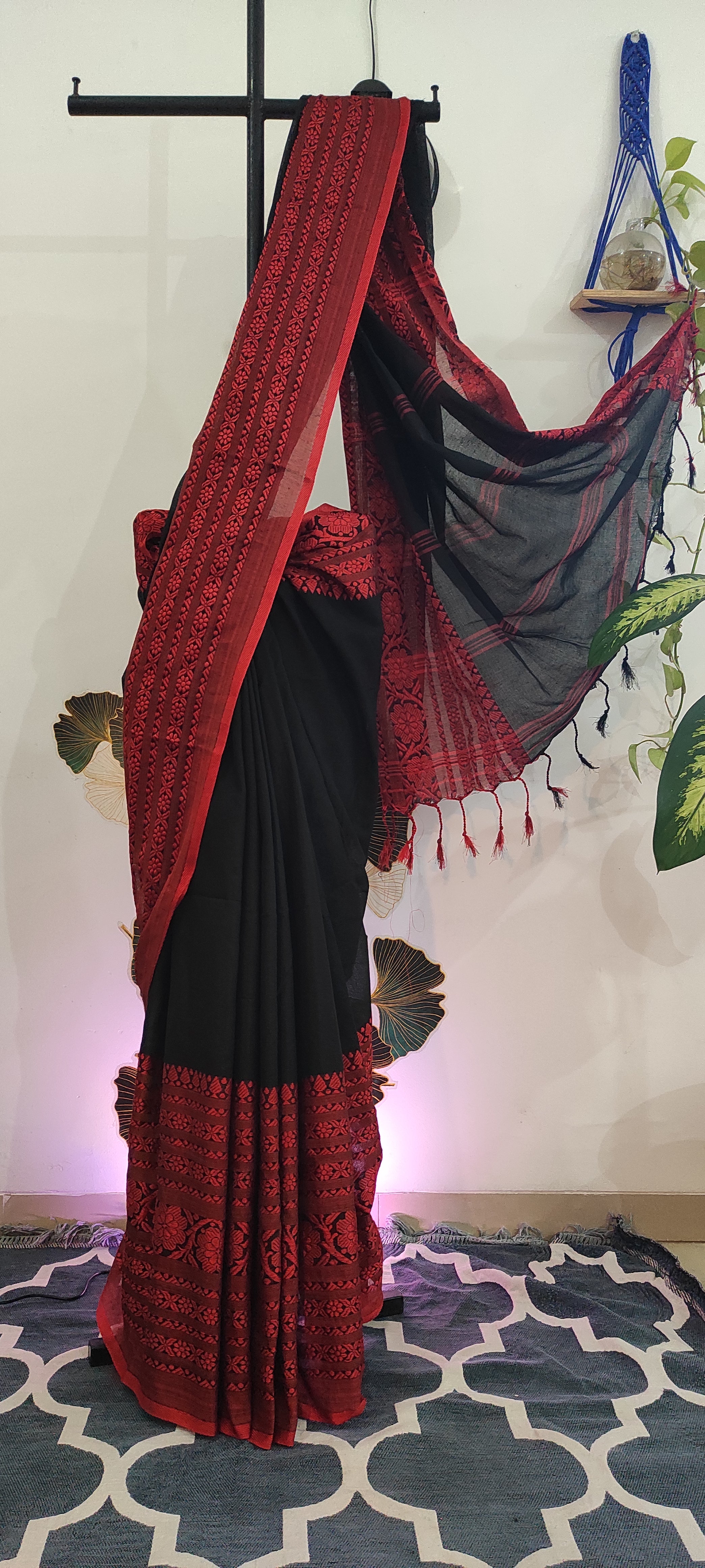 Red and black saree displayed on a stand against a patterned wall.