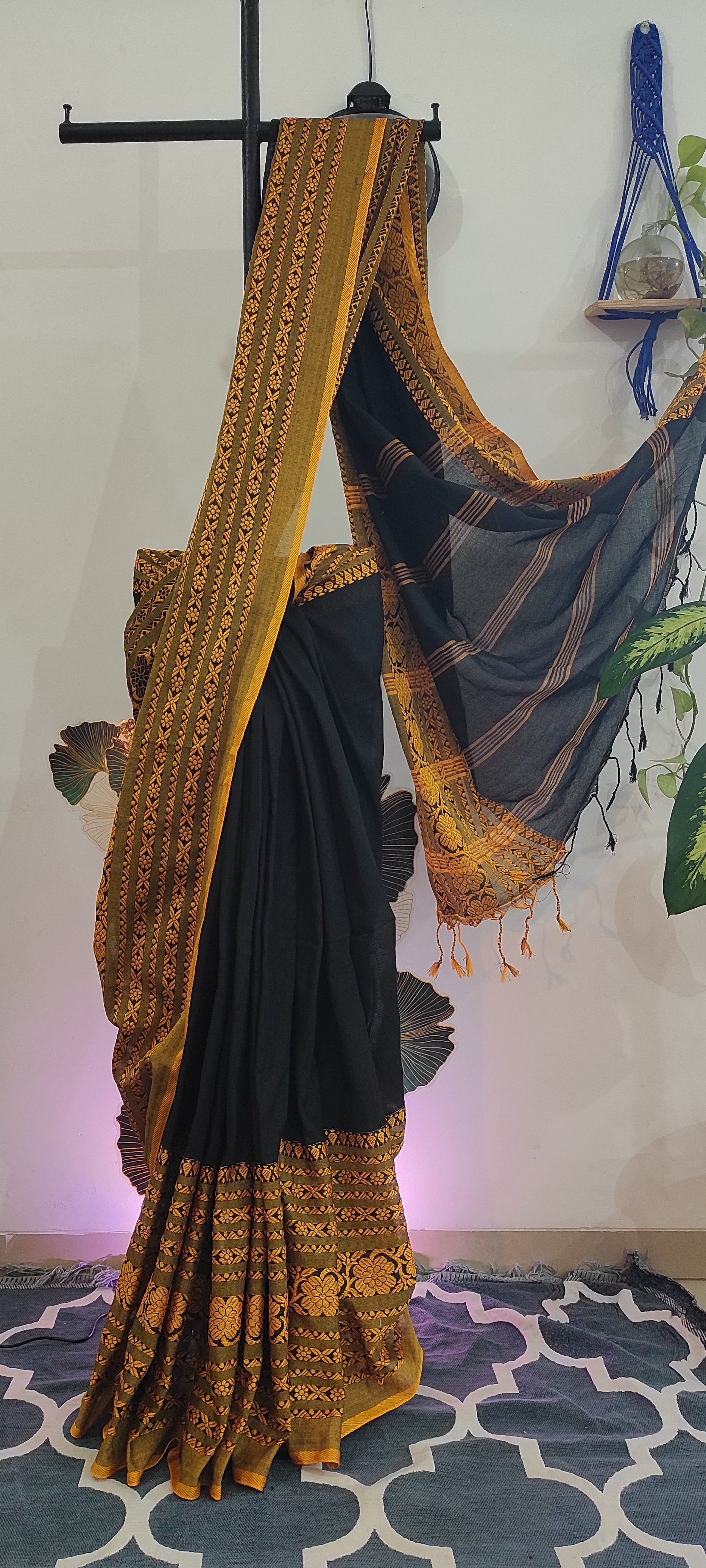 Black saree with gold embroidery on a stand against a colorful background