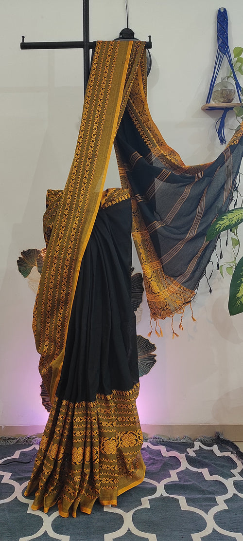 Black saree with gold embroidery on a stand against a colorful background
