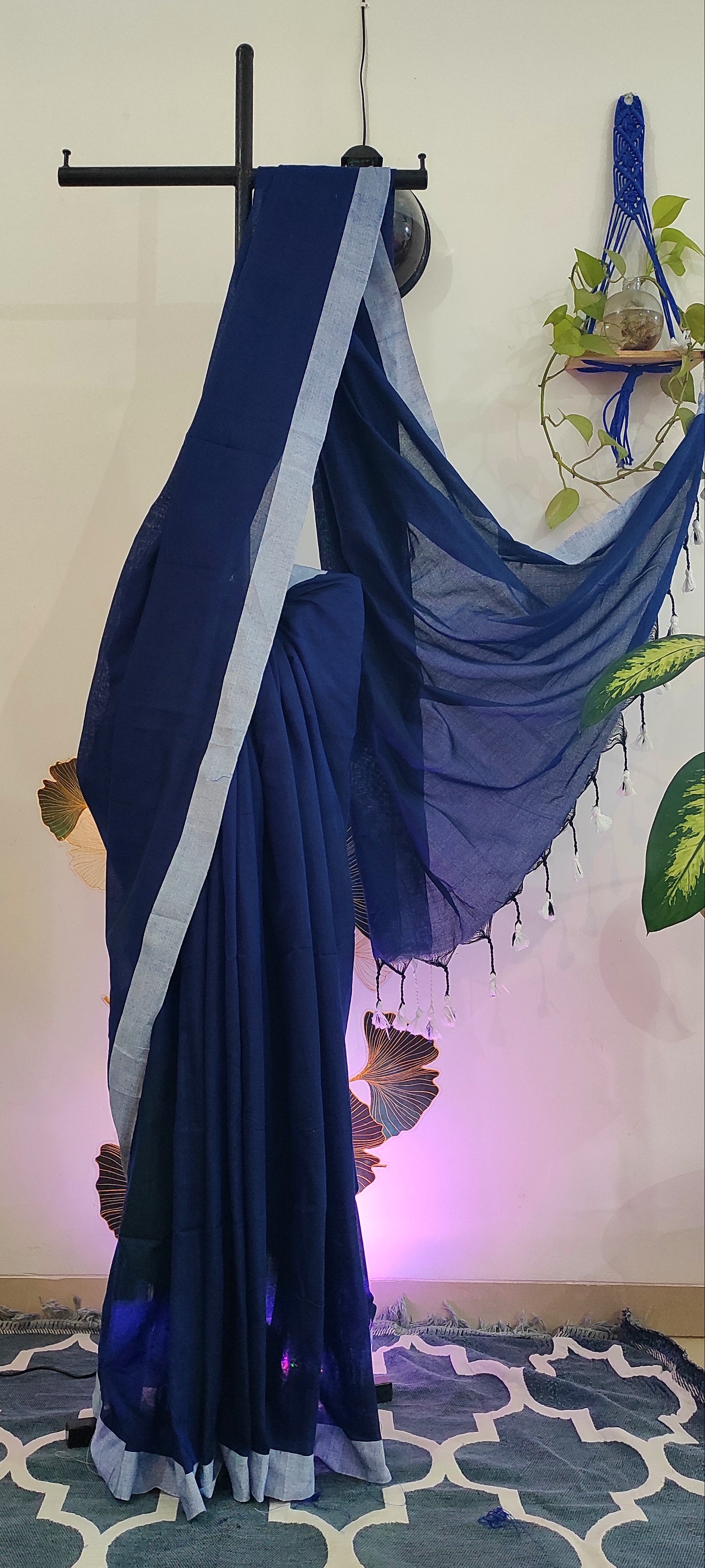 A blue saree with light blue border draped on a stand against a wall