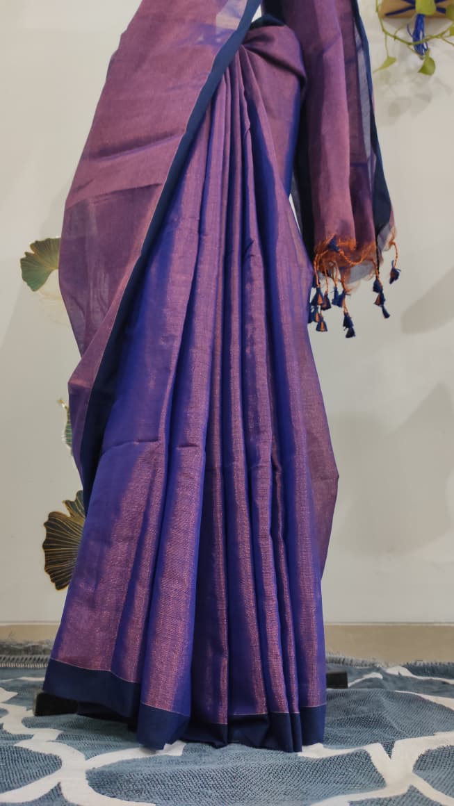 Tissue silk handloom saree draped on a saree stand which is purple in colour with copper shimmer and blue tassels